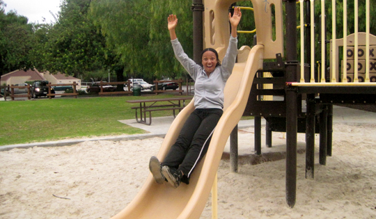 a woman sliding down a slide at a park