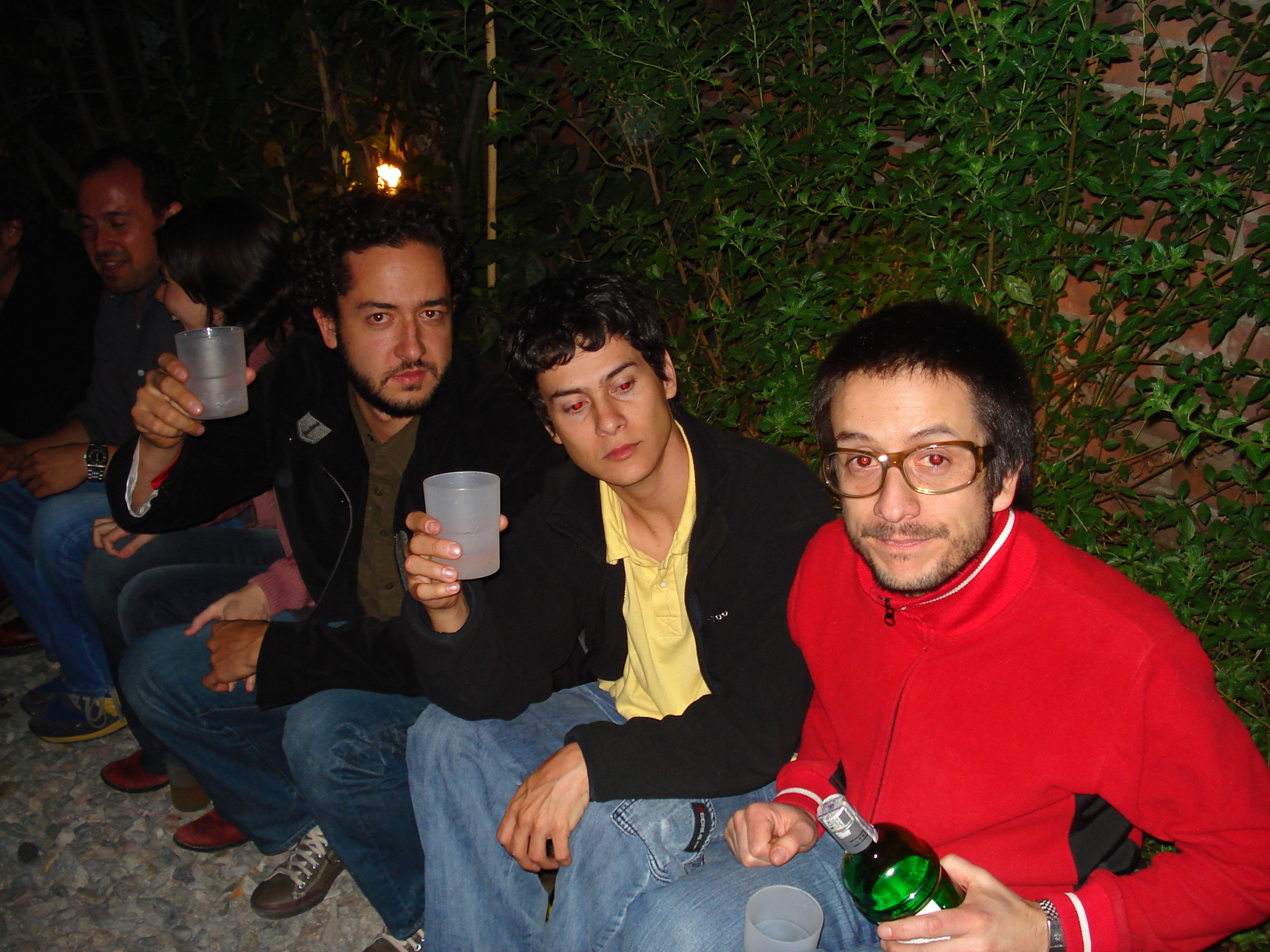 four men posing in front of a bush holding drinks