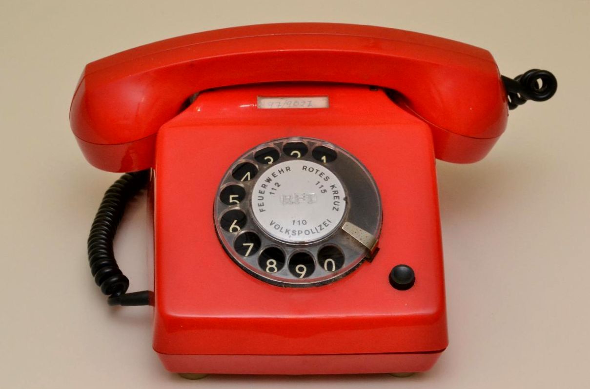 a red rotary telephone with no ons and two hands