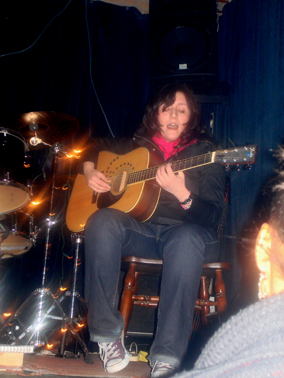 woman playing guitar while people watch from behind