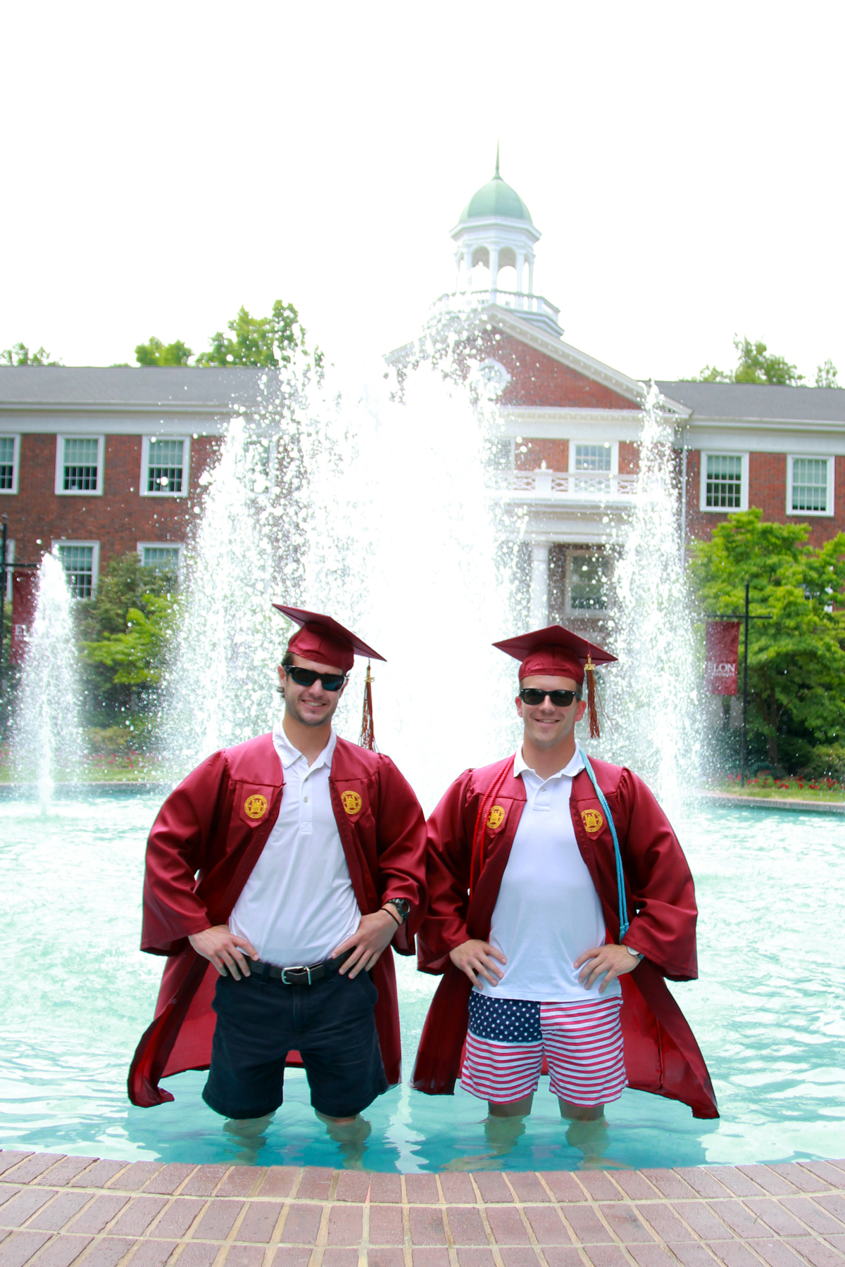 two people in graduation gowns standing next to a fountain