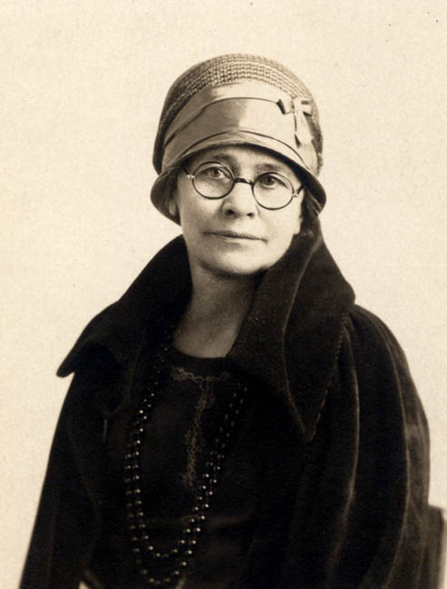 a woman wearing a hat, coat and glasses is posing for the camera