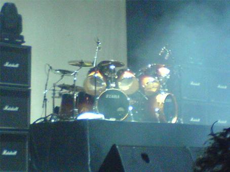 an empty stage has some drums, and some dark smoke