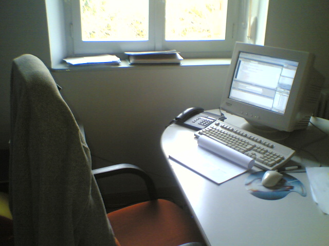 a chair and desk by the window with a keyboard, monitor and computer mouse