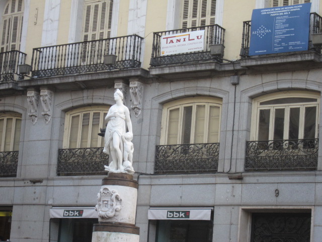 the statue on the corner of the building has a man standing in front