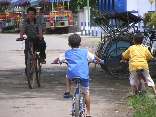 three boys ride bicycles in the middle of a dirt road