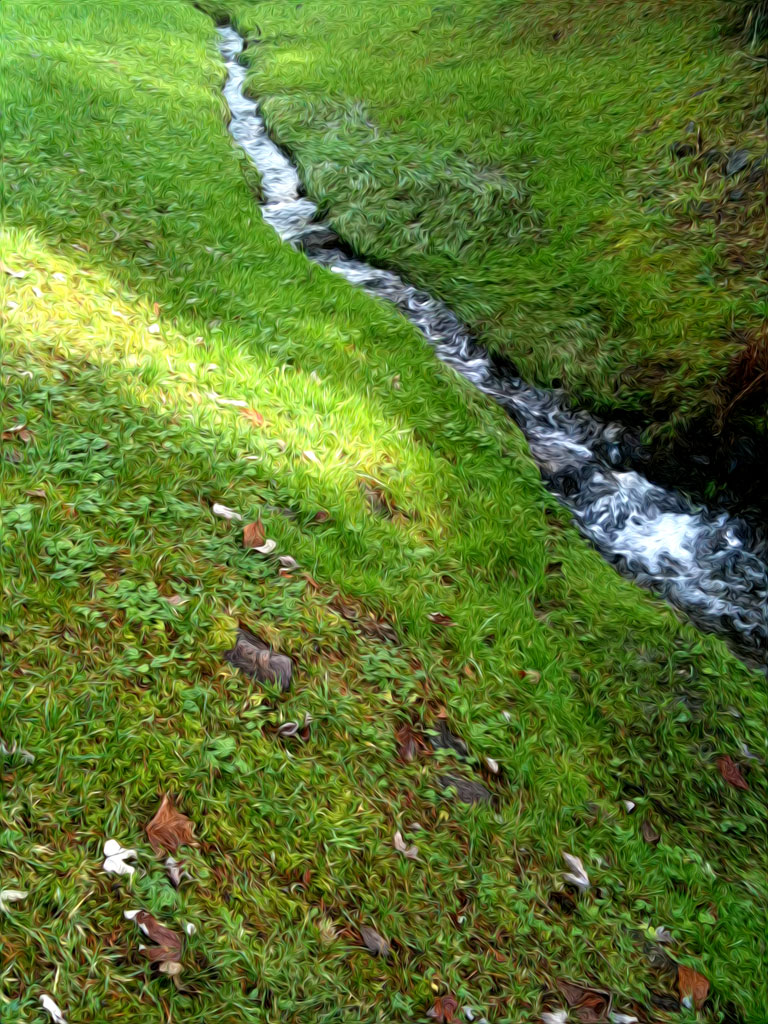 a creek running over green grass between two mountains