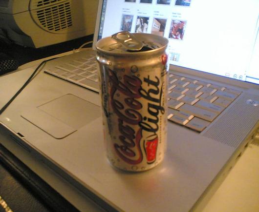 a can of soda sitting on top of an open laptop