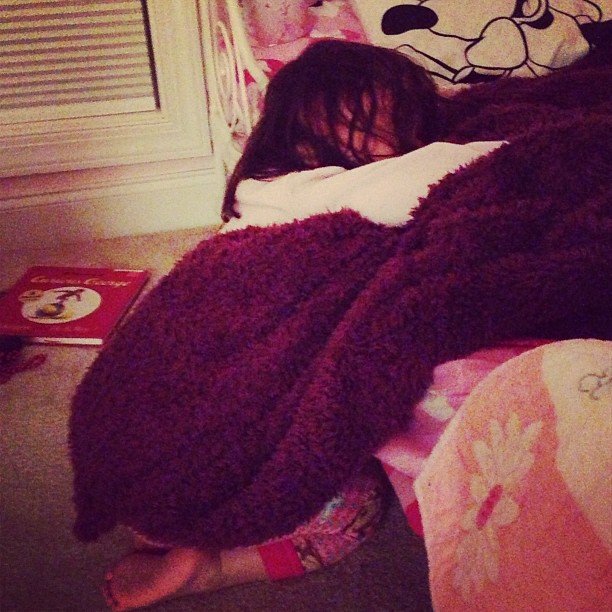 a little girl that is laying in bed under a blanket