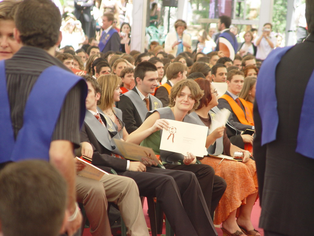 an audience at a ceremony dressed in graduation attire and holding up a sign