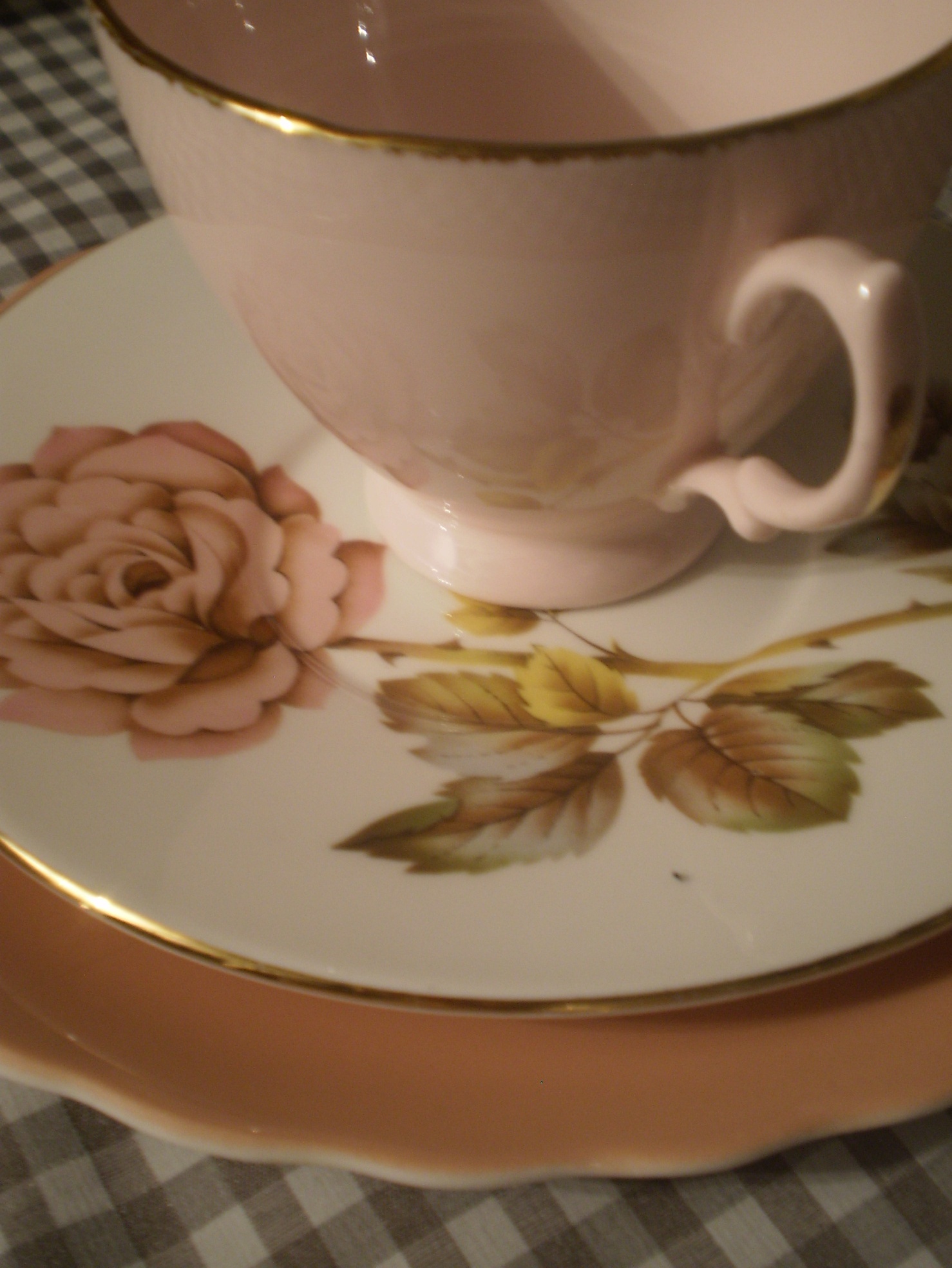 a pink rose on a white coffee cup sitting on a gold - rimmed saucer