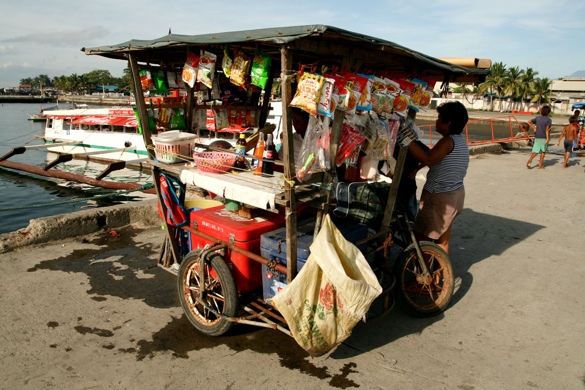 a man with a bicycle buying goods by a dock