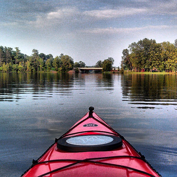 a red kayak floats across calm water on a partly cloudy day