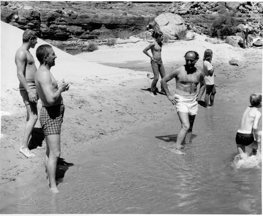 some guys and one girl in trunks are playing in the water on the beach