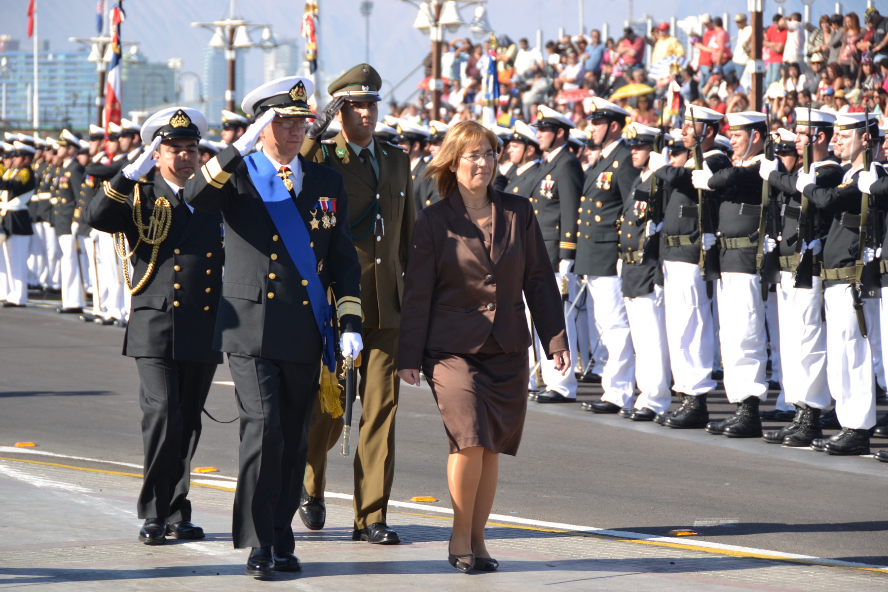 a man in uniform and a woman walking down the street next to a line of uniformed people