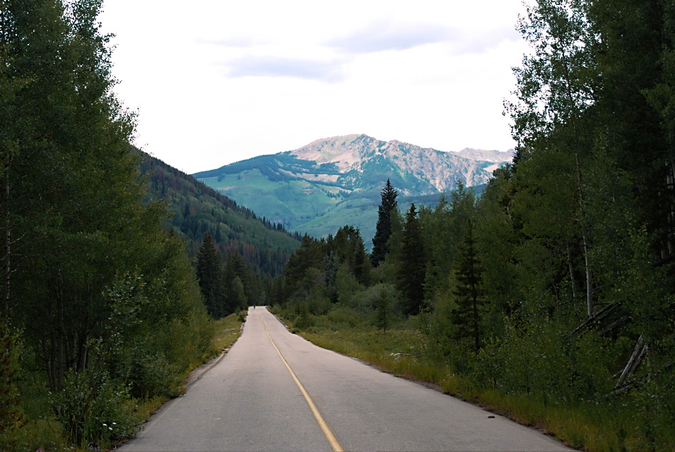 an empty road leads into the distance in front of a mountain