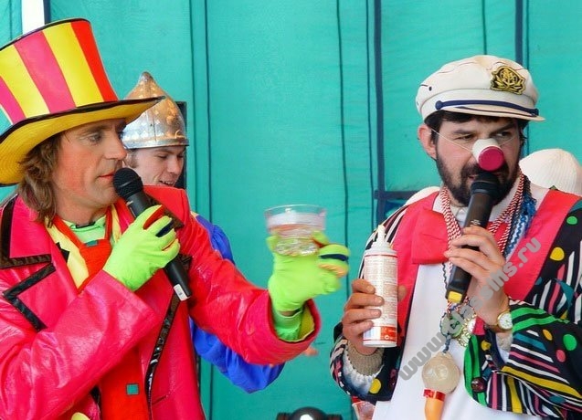 two people with hats and colorful costumes on one holding a glass of liquid