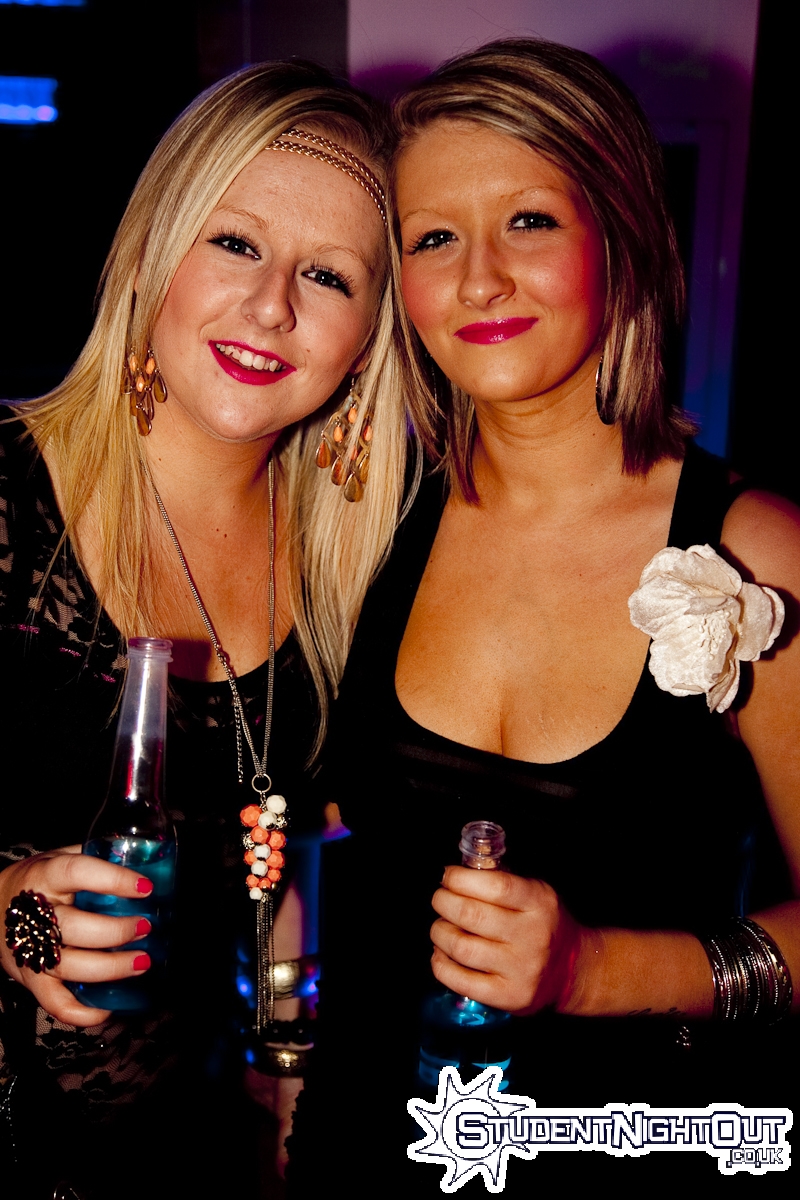 two ladies are smiling and drinking together at an event