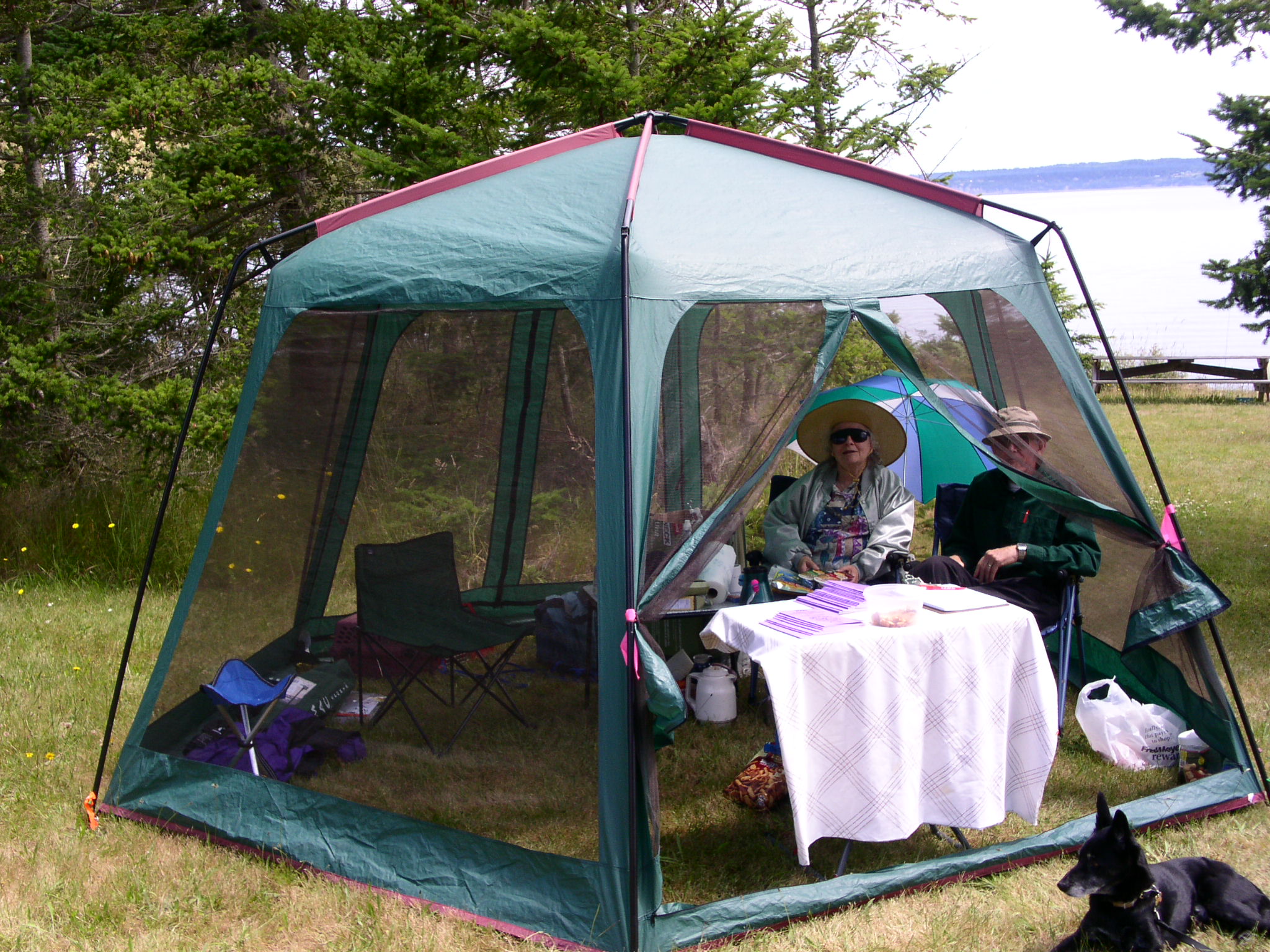 two people in a tent setting with a dog sitting by the side of it