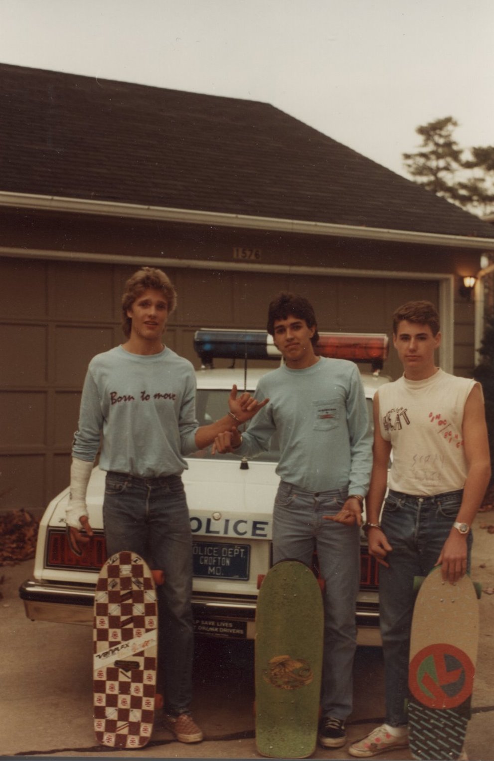 three young men are holding skateboards by a car