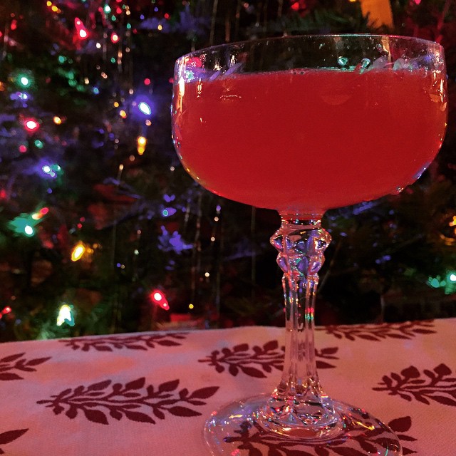 a glass of wine sits on a table with a christmas tree in the background