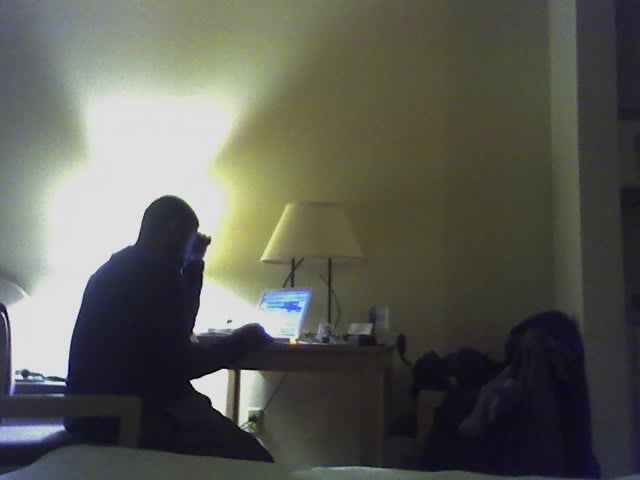 a man sitting on his bed using his laptop and talking on the phone
