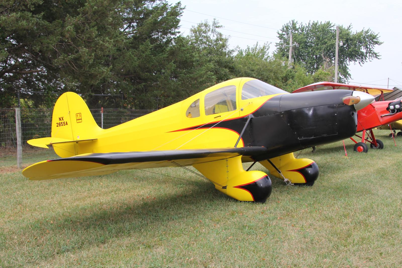 a small yellow plane sitting in the grass next to a red and black airplane