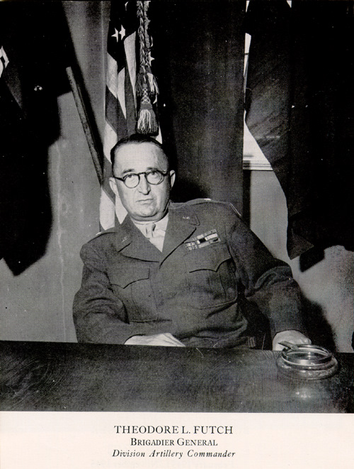 a man sitting at a desk with several flags behind him