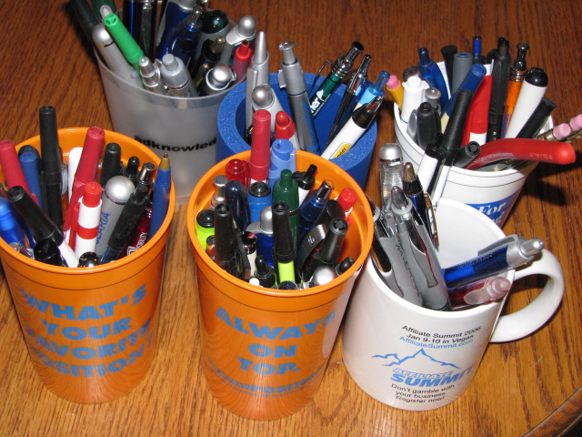 various pens, markers, and scissors are in cups