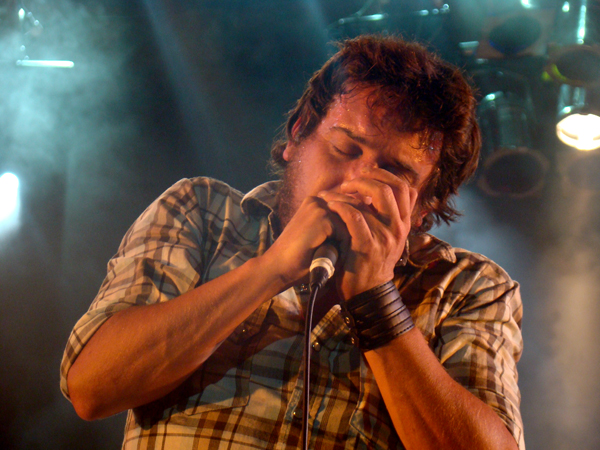 a man with long hair, in plaid shirt holding a microphone