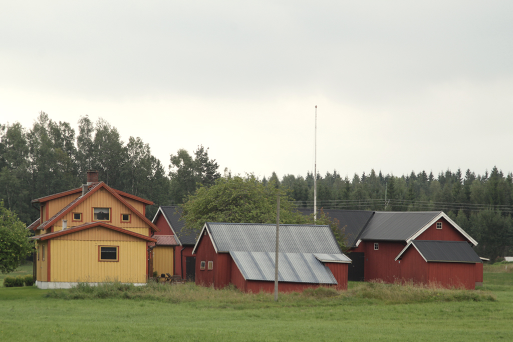three red buildings on grass near trees