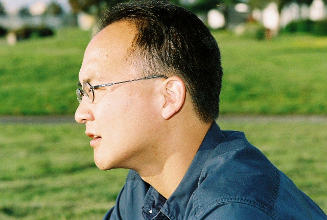 a man with a tie and glasses sitting in front of a green field