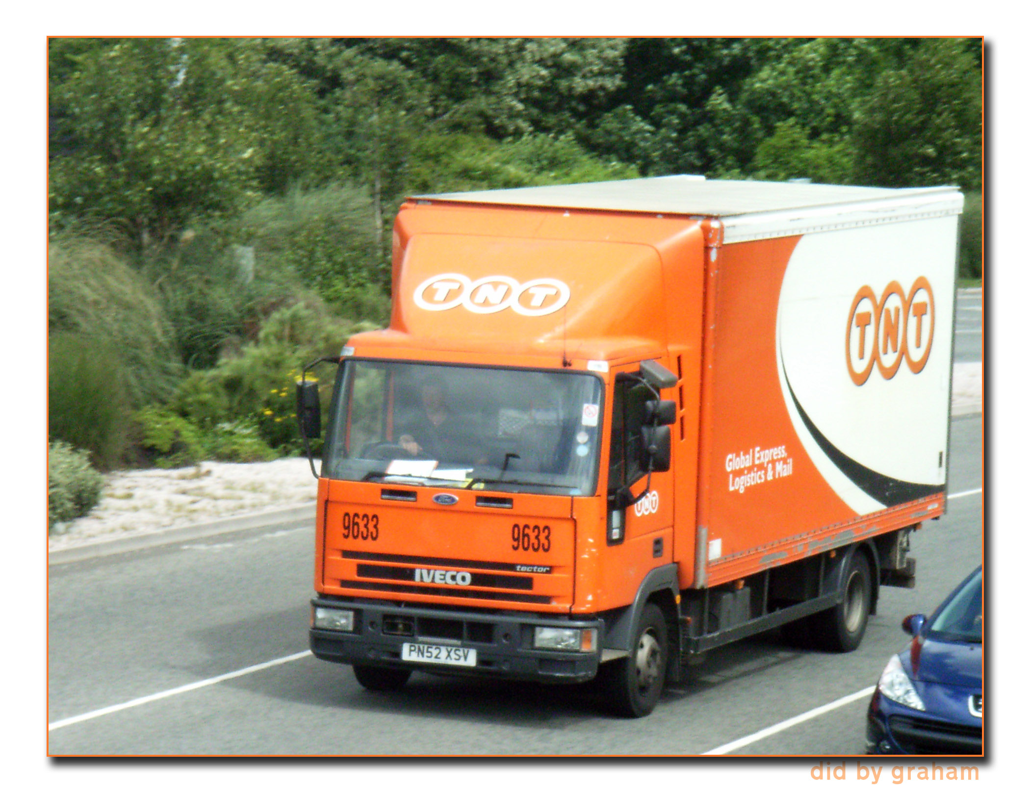 a red delivery truck traveling down a road next to trees