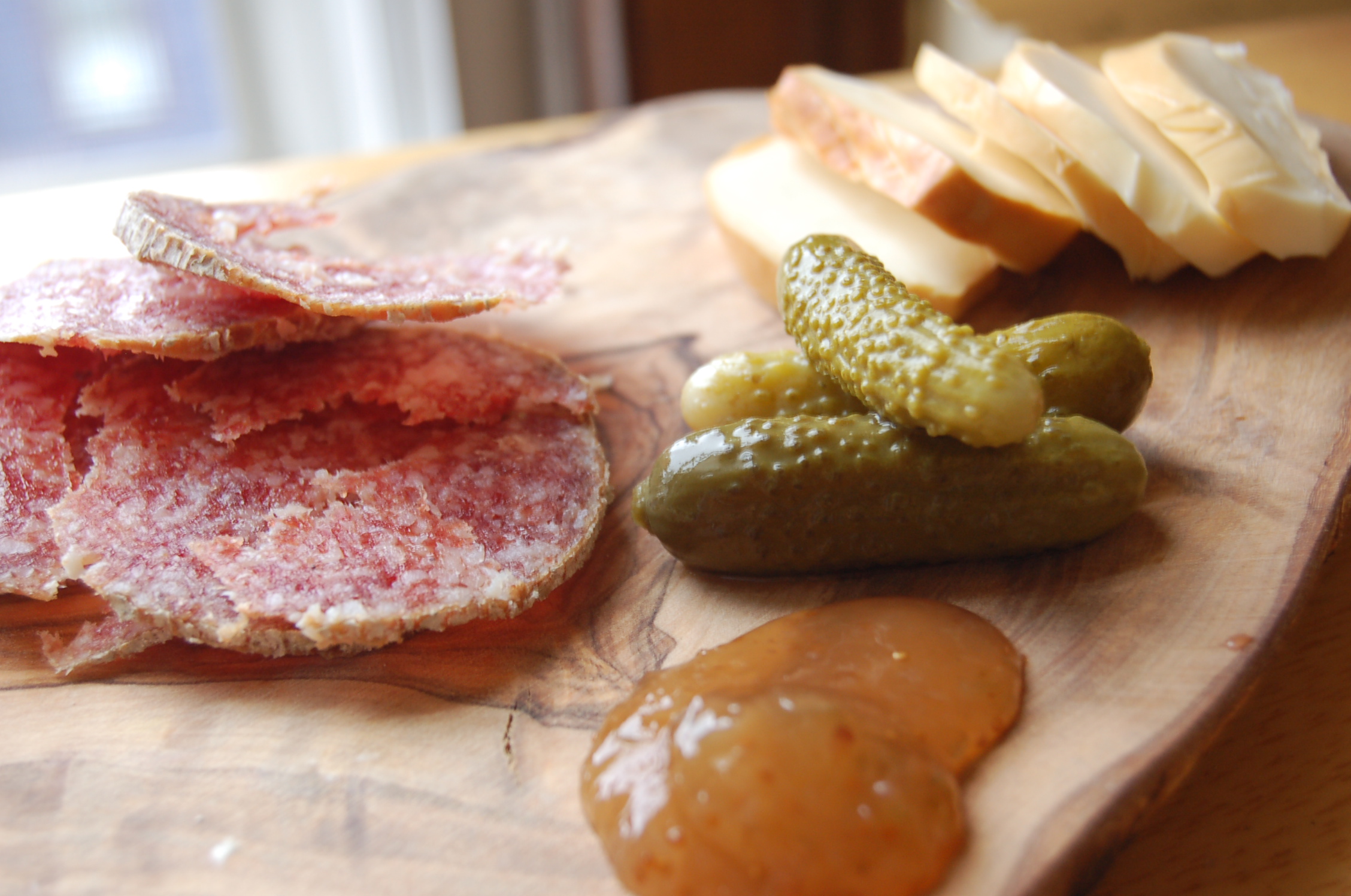 there is a wooden board with cheese, meat, and vegetables