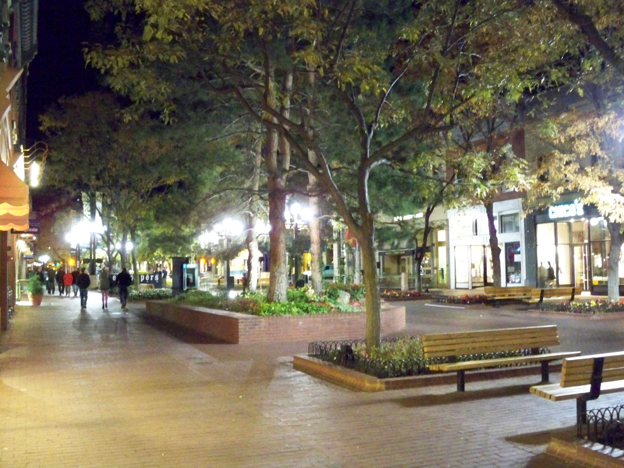 people walking down the sidewalk at night, in front of buildings