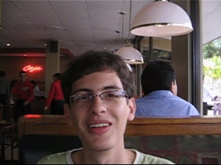 a boy with glasses and a tie in front of a pizza shop