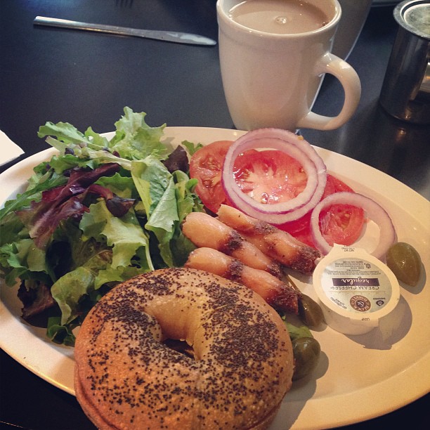 a bagel, salad, dressing and fruit on a plate