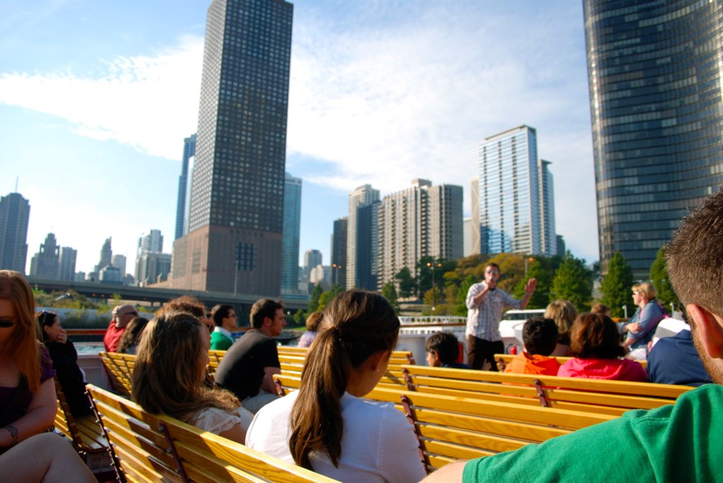 a number of people sitting on a wooden bench in a large city