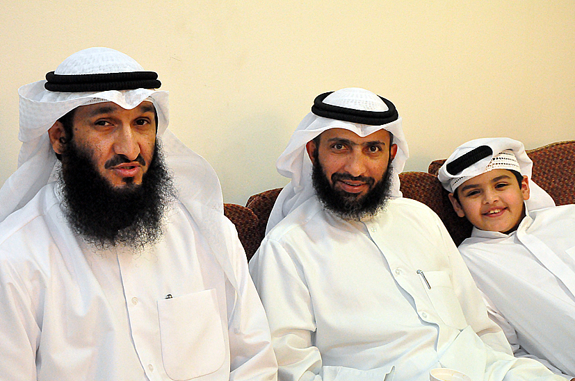 three men sitting side by side with one wearing a white outfit