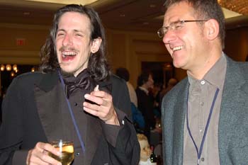 two men are smiling at one another while they hold wine glasses