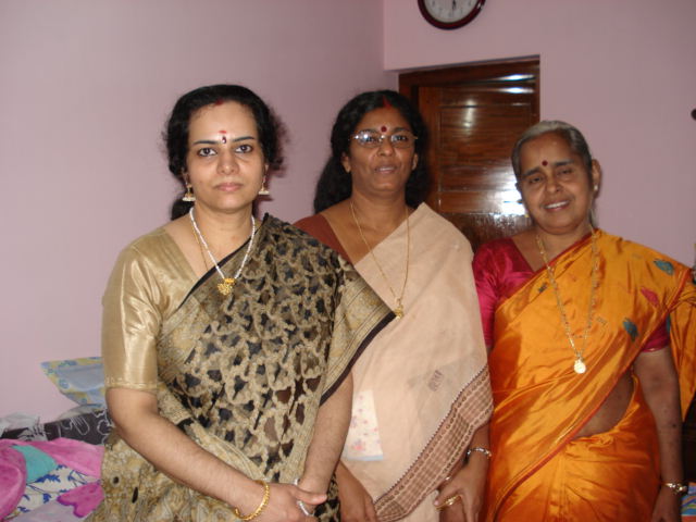 three women in sari standing on a bed with an older man