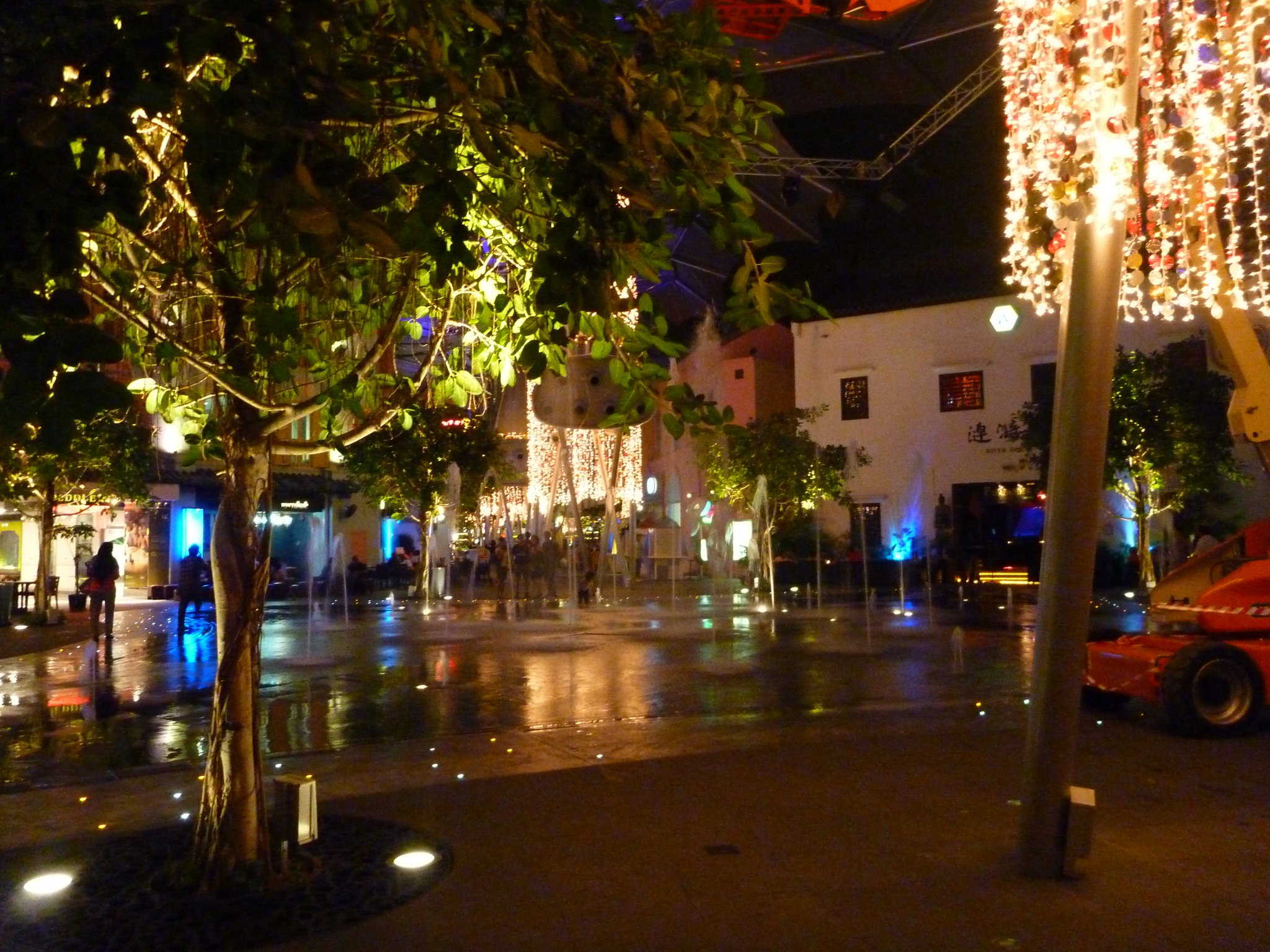 several trees are lit up at night on the wet sidewalk