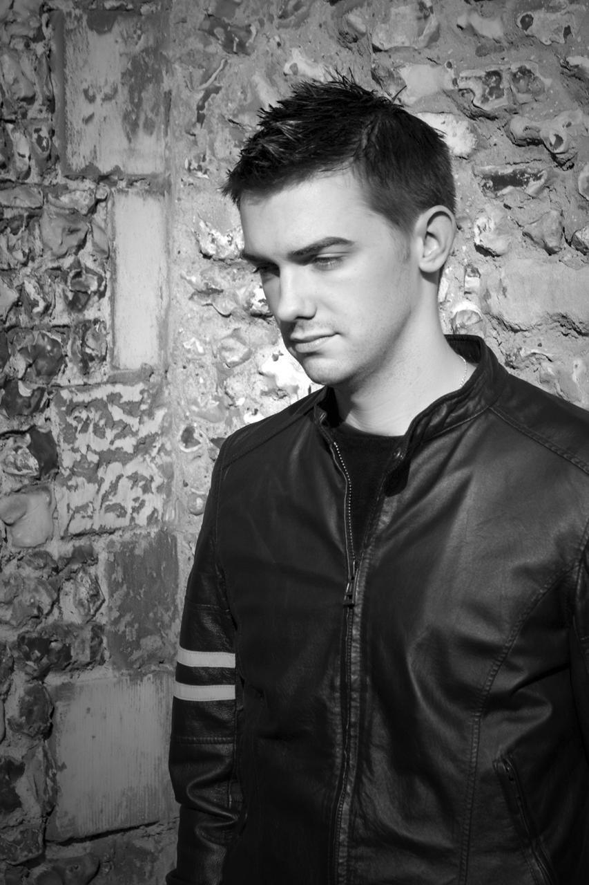 a man in a leather jacket standing next to a brick wall