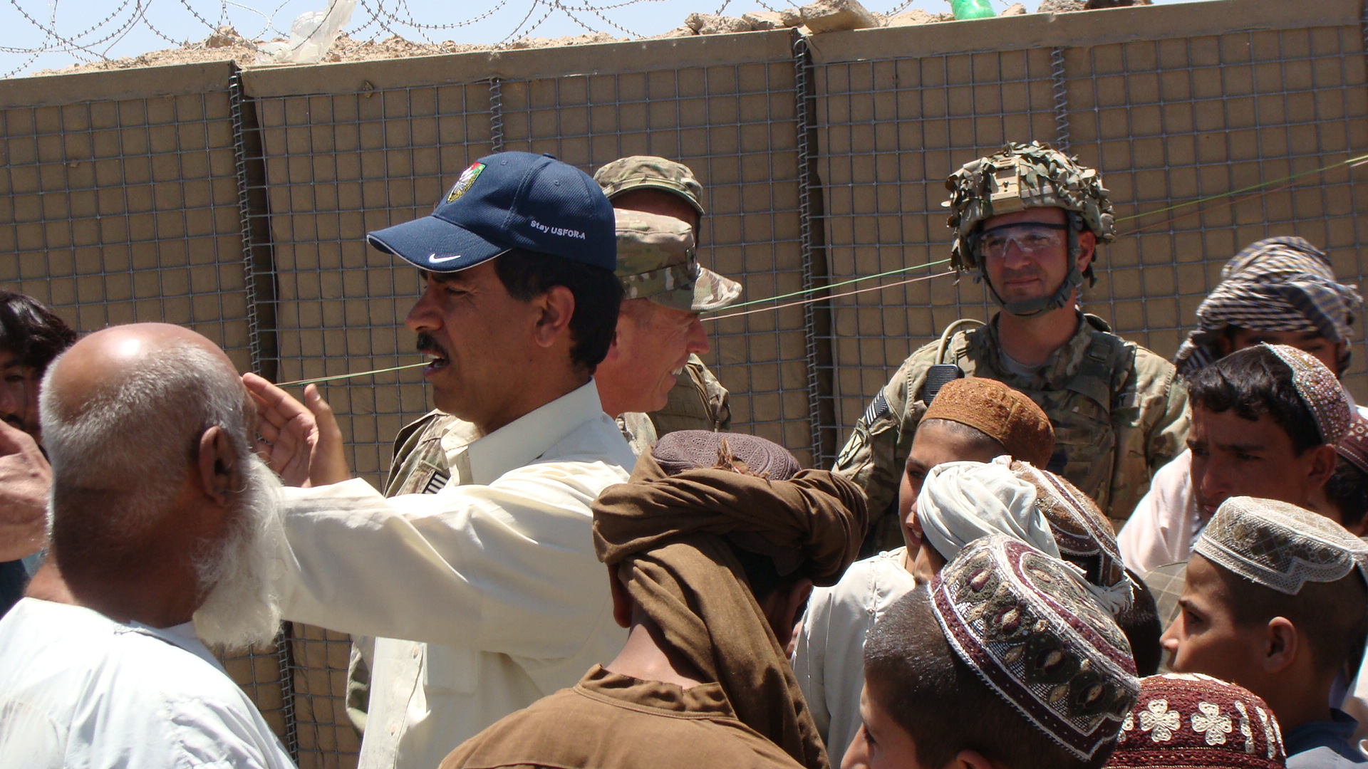 men in military garb stand near a fence and stare at soing