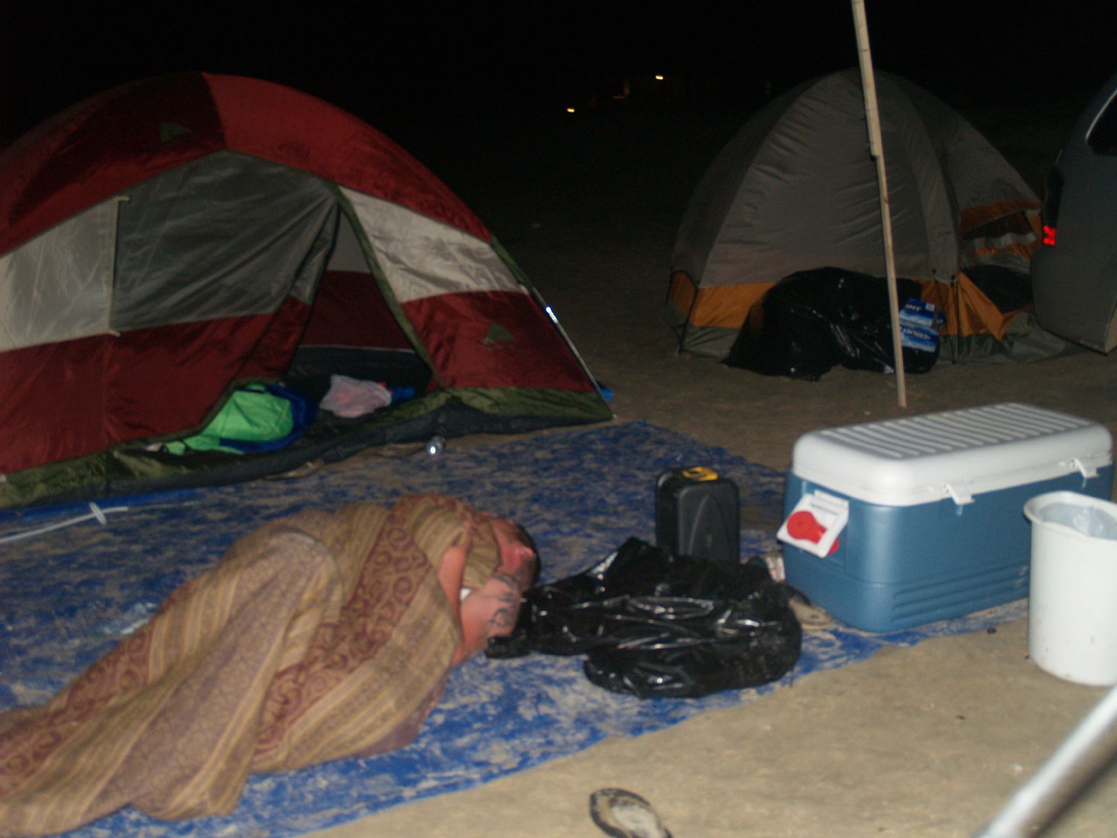 a man sleeping on the ground in front of several tents
