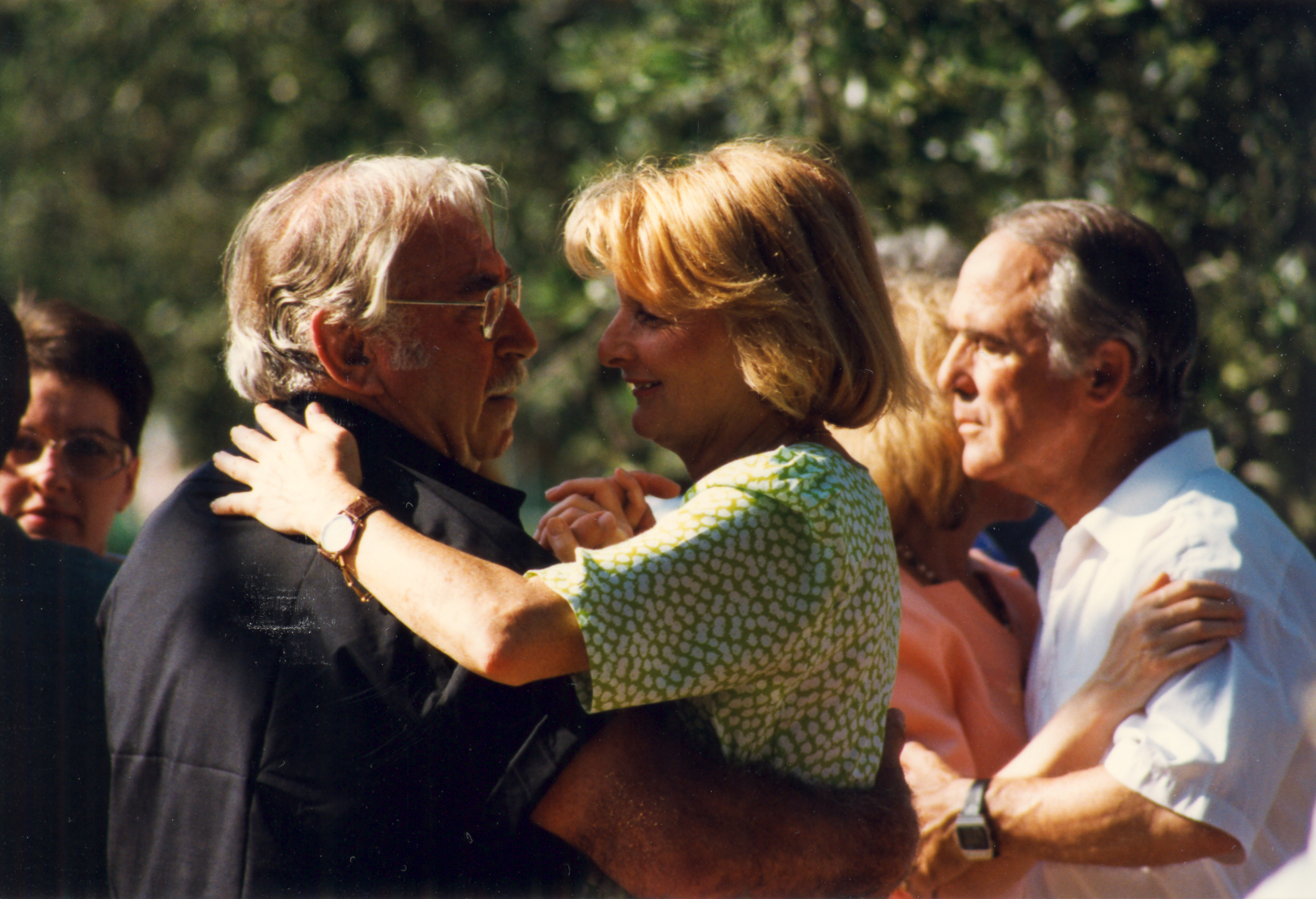two women hugging and a man with glasses standing in front of them