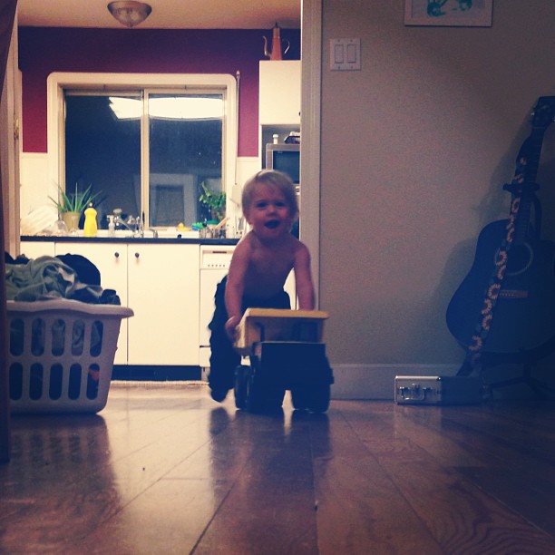 young child carrying cart on wooden floor in room