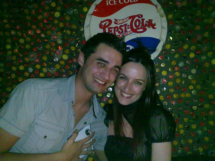 a man and a woman standing together in front of a coca cola sign