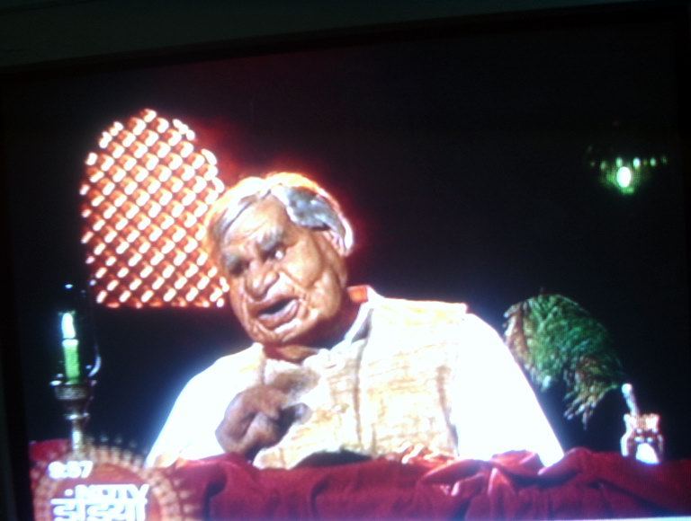 a screen s shows a man sitting down in front of a tv with a pattern on it