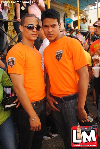 two men in orange shirts stand near a crowd